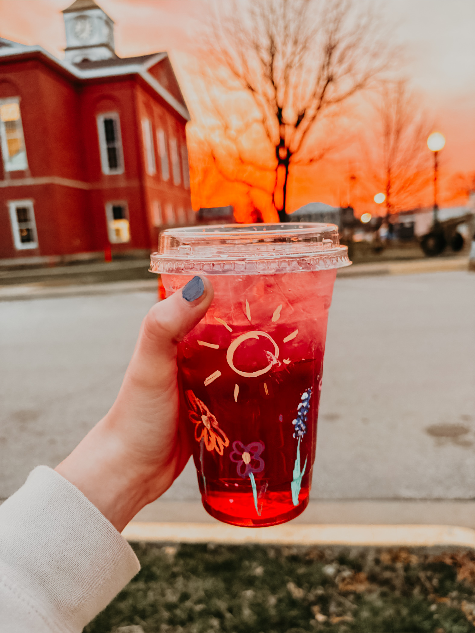 A hand-painted lotus drink held up at sunset in front of the Versailles courthouse