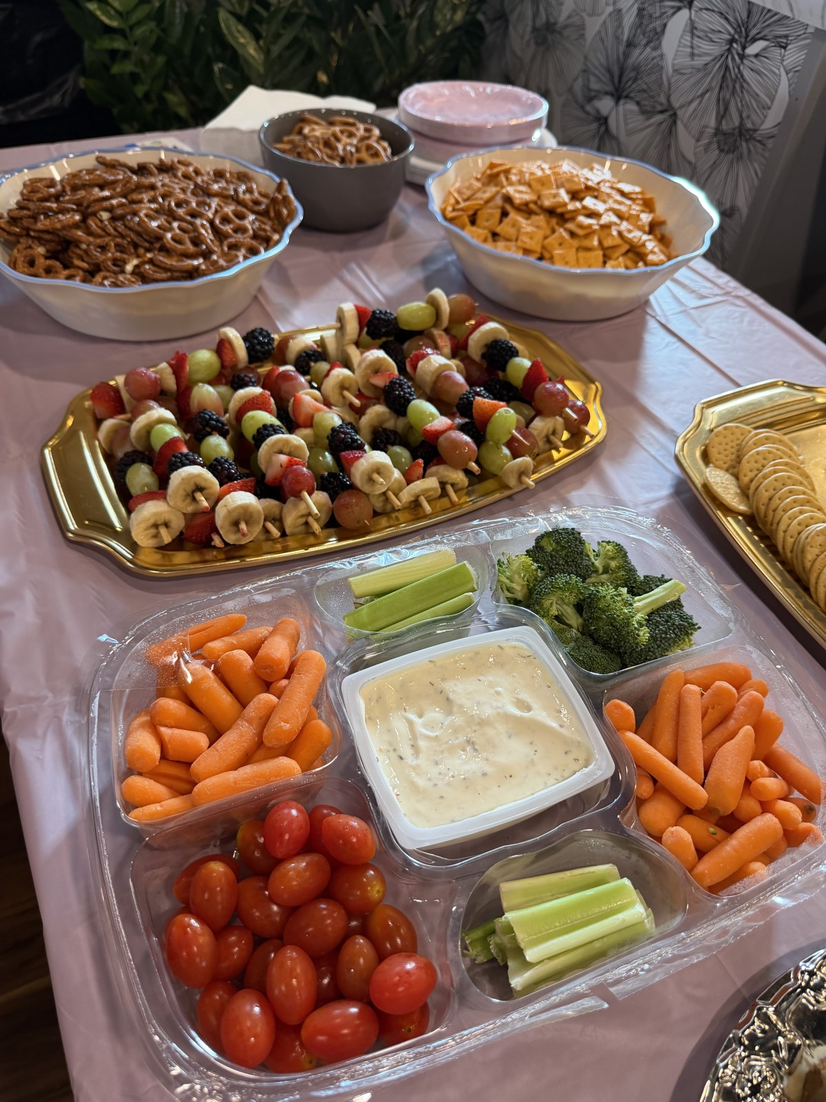 A party snack table with fruit skewers, veggie tray, pretzels and crackers